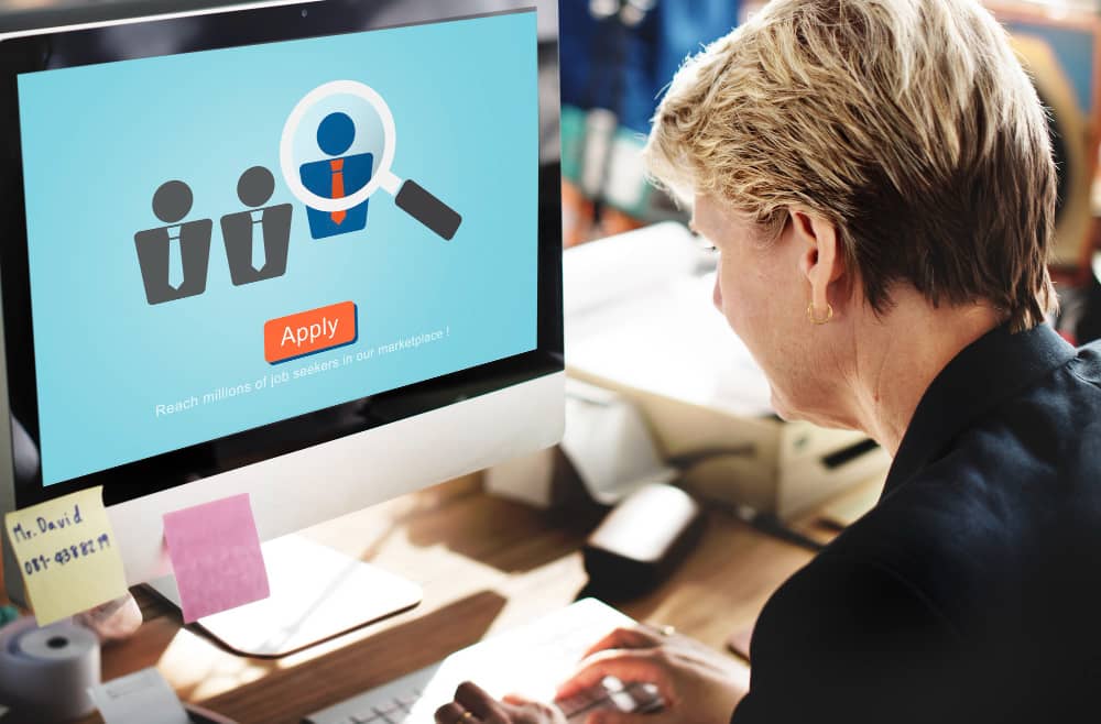 HR professional viewing an applicant tracking system on a computer screen with a magnifying glass over a candidate icon.