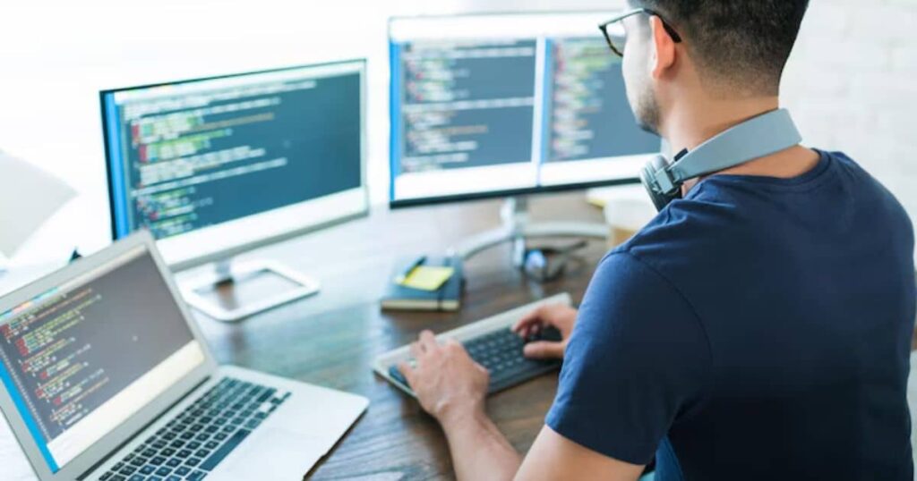 A developer working at a desk with multiple monitors displaying code and a laptop, wearing a headset.